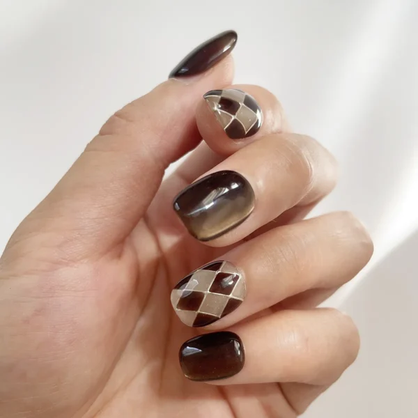 Left hand modeling chocolate brown and nude cat eye fake nails with argyle pattern