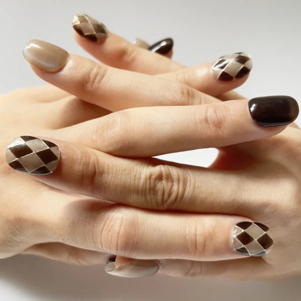 Hand wearing trendy short brown and nude cat eye fake nails with argyle pattern