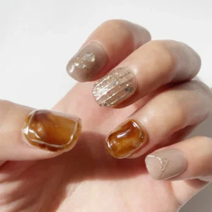 Left hand modeling amber tortoiseshell and nude fake nails with gold detailing and pearl shimmer