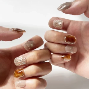 Amber tortoiseshell and nude fake nails with gold detailing and pearl shimmer on finger