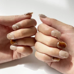 Hand wearing trendy short amber tortoiseshell and nude fake nails with gold detailing and pearl shimmer