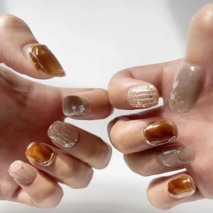 Close-up of amber tortoiseshell and nude press-on nails with gold detailing and pearl shimmer