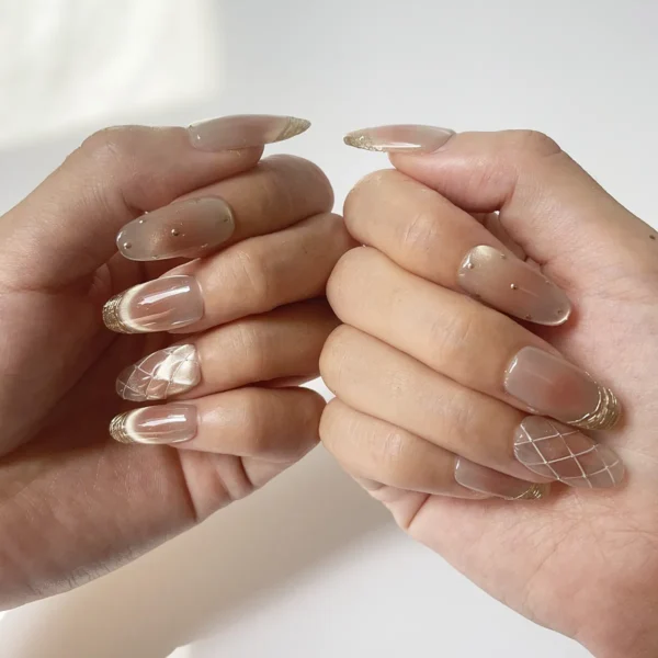 Close-up of long oval rose gold-pink cat eye fake nails with gold French tips, quilted and polka dot accents